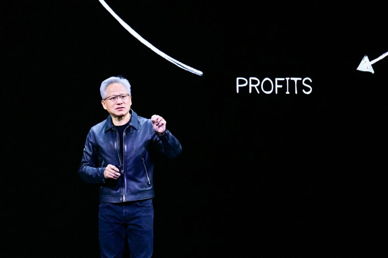 Jensen Huang speaks on stage, the screen behind him is black, with white text that reads "PROFITS"